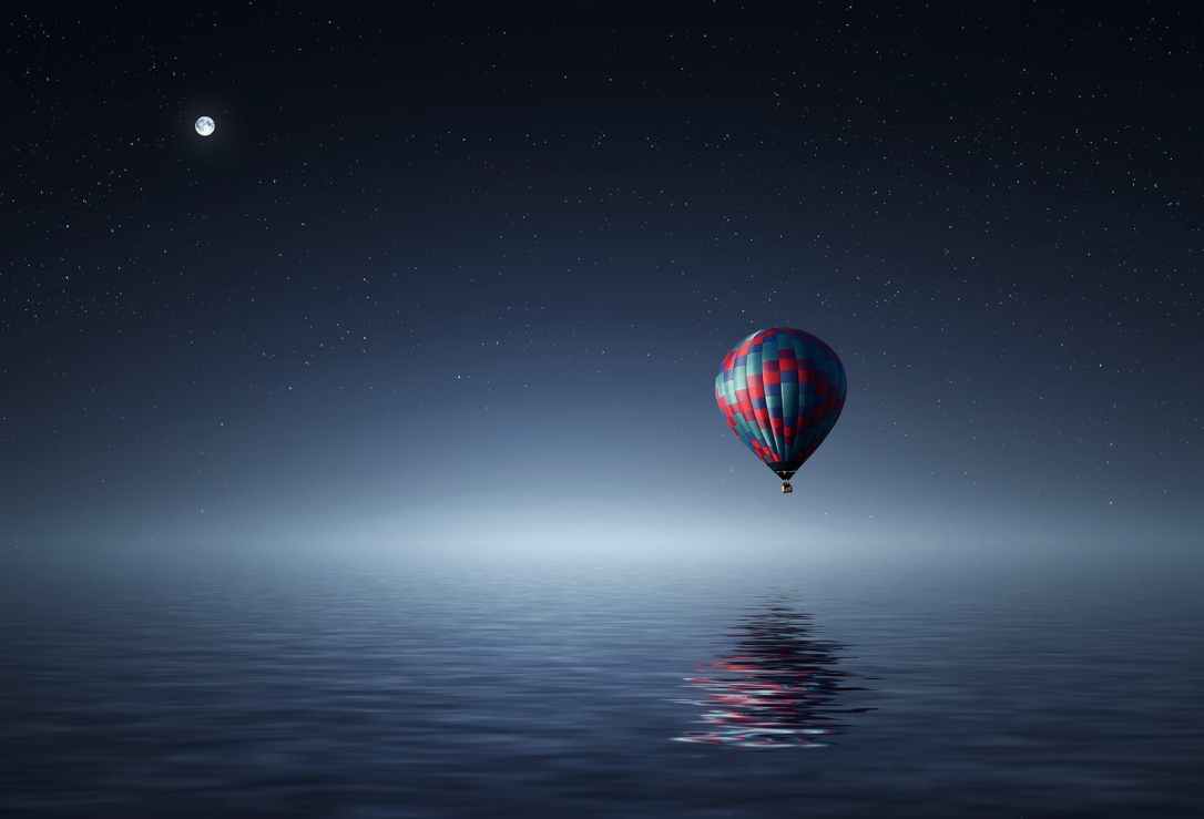 red and blue hot air balloon floating on air on body of water during night time